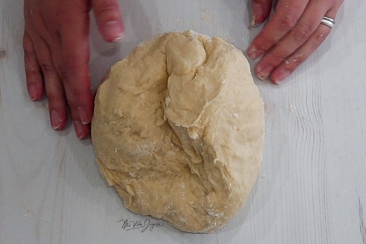 Una bola de masa sobre una encimera con dos manos, una a cada lado de la masa.