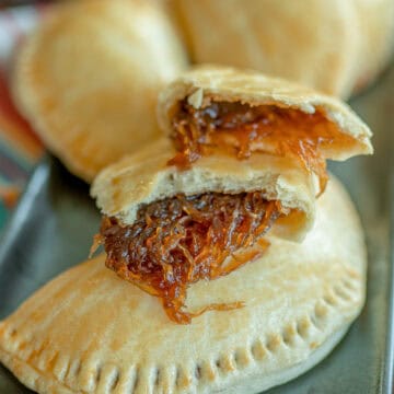 Un plato con varias empanadas de chiverre cocinadas, mientras una por encima se encuentra partida a la mitas y se muestra el relleno de chiverre.