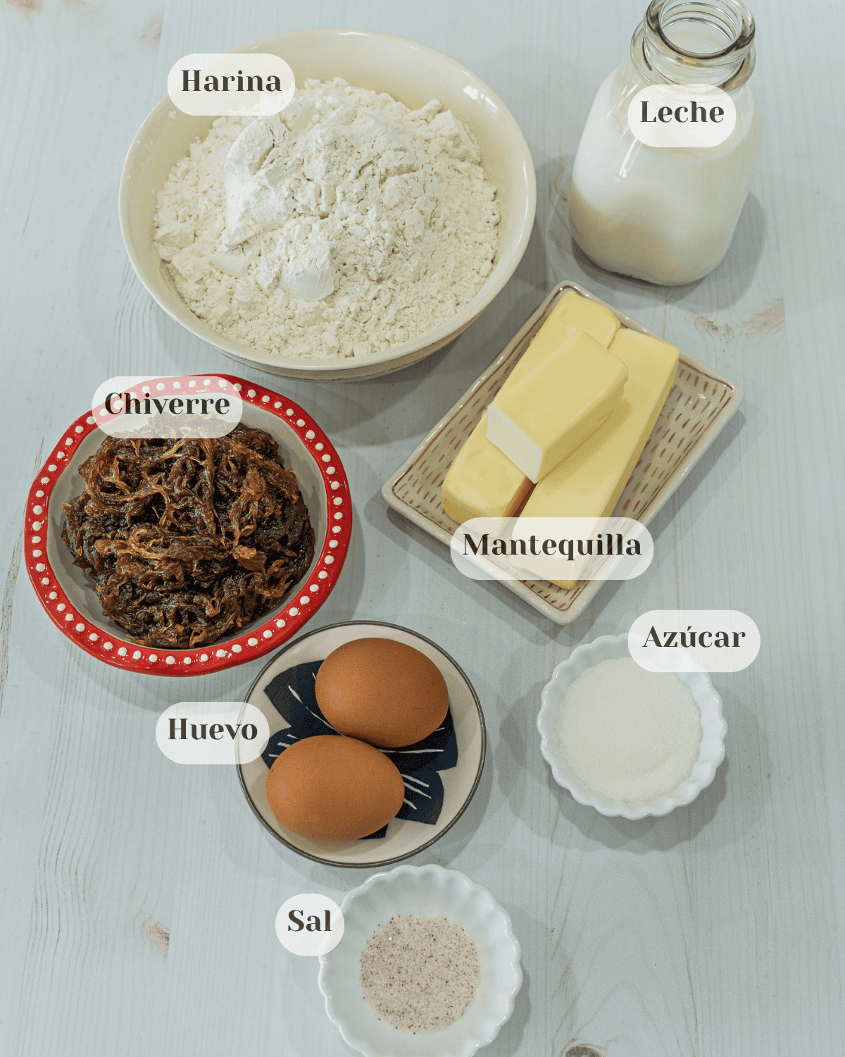 Una foto de todos los ingredeintes colocados en tacitas: La harina, la leche, una tacita de chiverre en miel, dos barras y media de mantequilla, dos huevos, una tacita con azúcar y otra con sal.