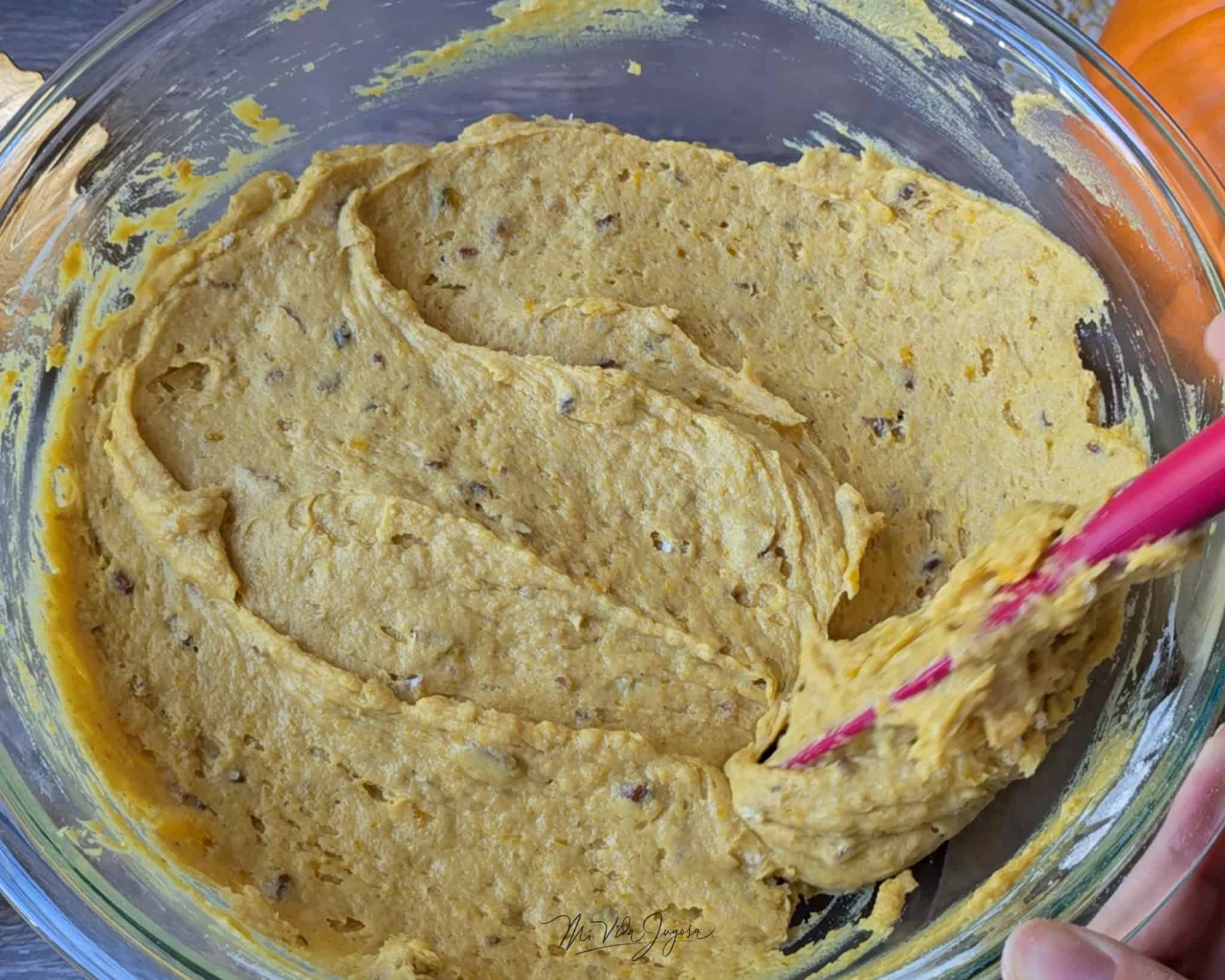 Tazón de vidrio con la mezcla del queque de calabaza y pedacitos de pecanas, siendo revuelta con una espátula