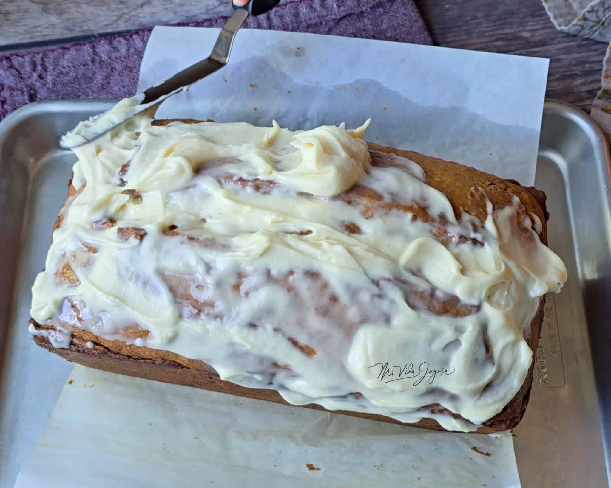 Queque de calabaza decorado con glaseado de queso crema y miel de maple, colocado sobre una bandeja plana y un papel encerado.