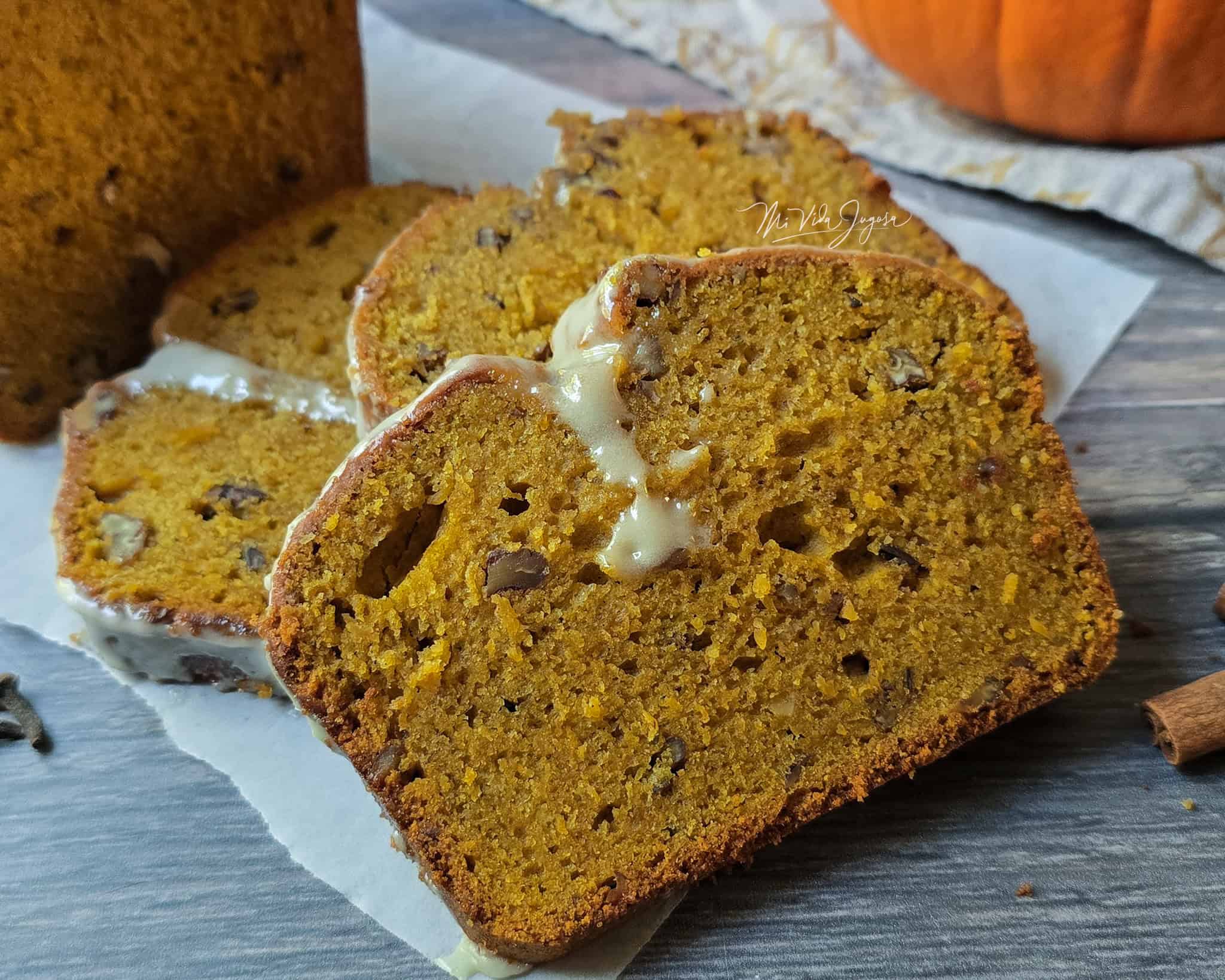 Tres rebanadas de queque de calabaza colocadas una sobre otra, con el resto del queque al fondo, todo sobre un pedazo de papel encerado.
