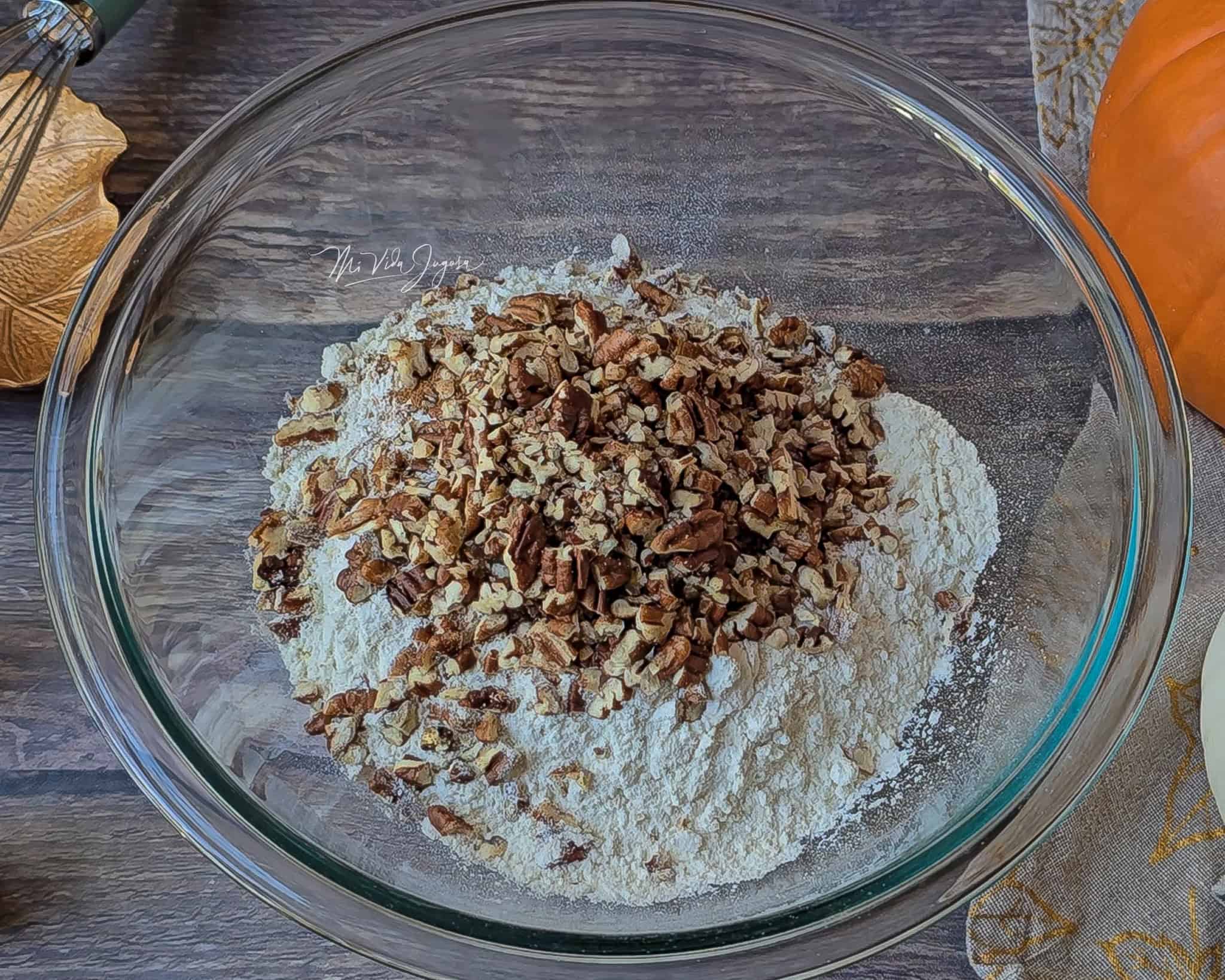 Tazón de vidrio con harina y pecanas picadas por encima