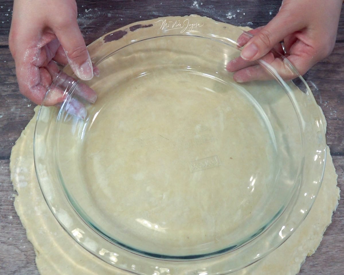 Unas manos sostienen un molde para pay sobre una masa extendida.