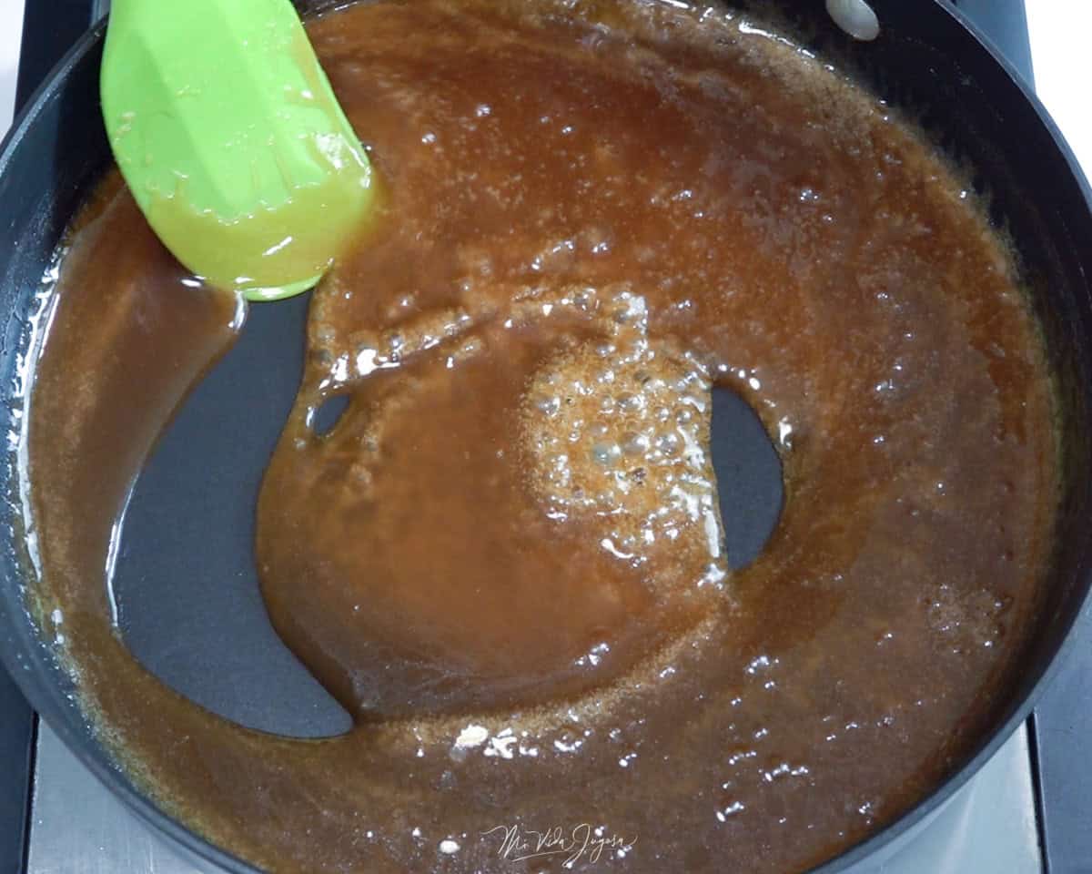Un sartén con una espátula revolviendo la mezcla de mantequilla y azúcar moreno, y jugo de piña.
