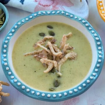 Un plato hondo con una cremosa crema de vegetales de color verde suave, decorada por encima con semillas de girasol y cebolla frita crujiente.