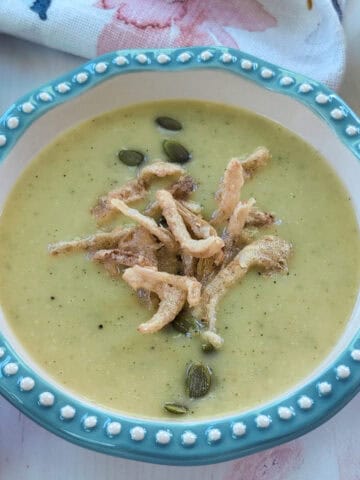 Un plato hondo con una cremosa crema de vegetales de color verde suave, decorada por encima con semillas de girasol y cebolla frita crujiente.