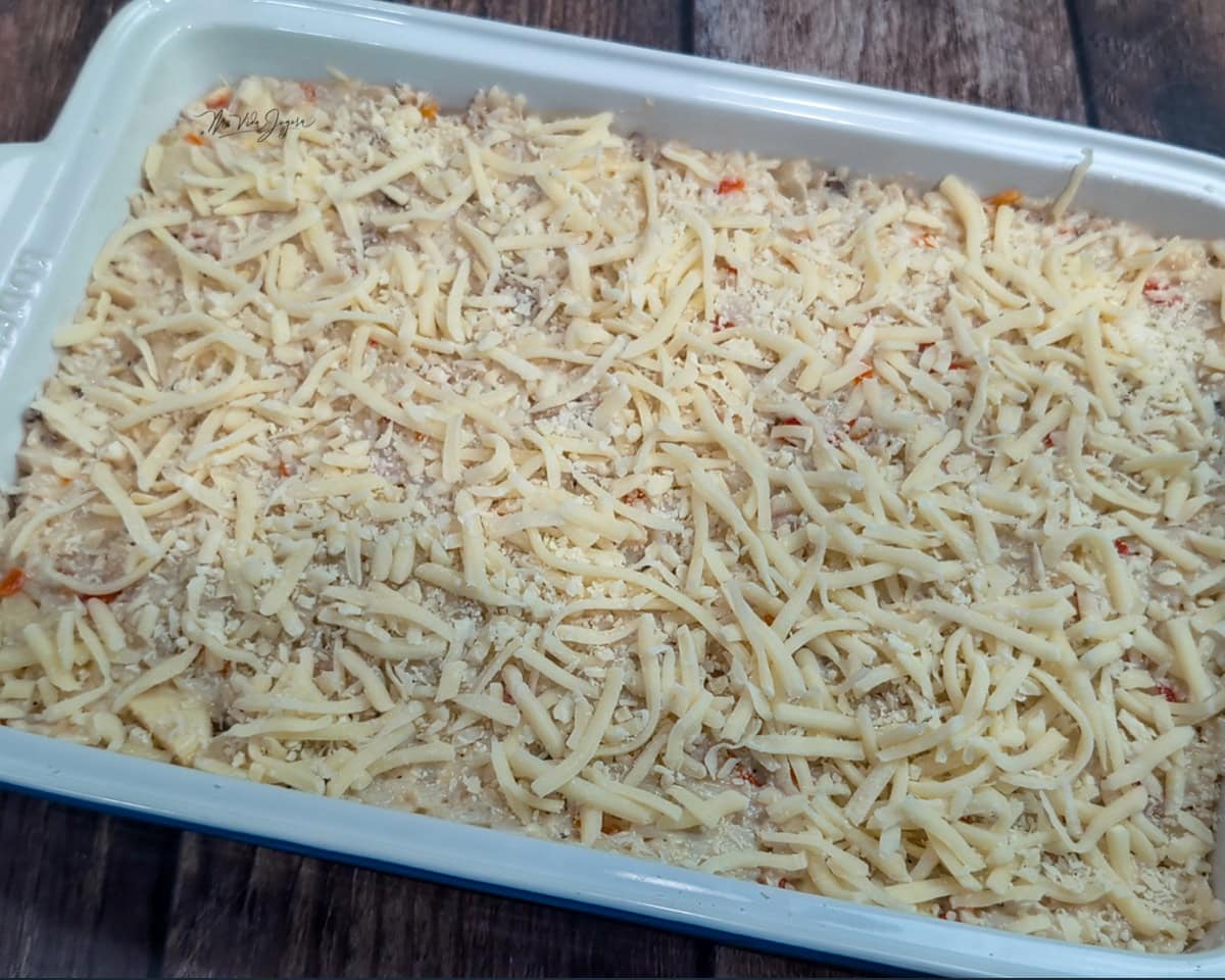 Un pyrex blanco cuadrado que contiene la mezcla del arroz con palmito sin ser horneado, se observa una capa de queso mozzarella por arriba