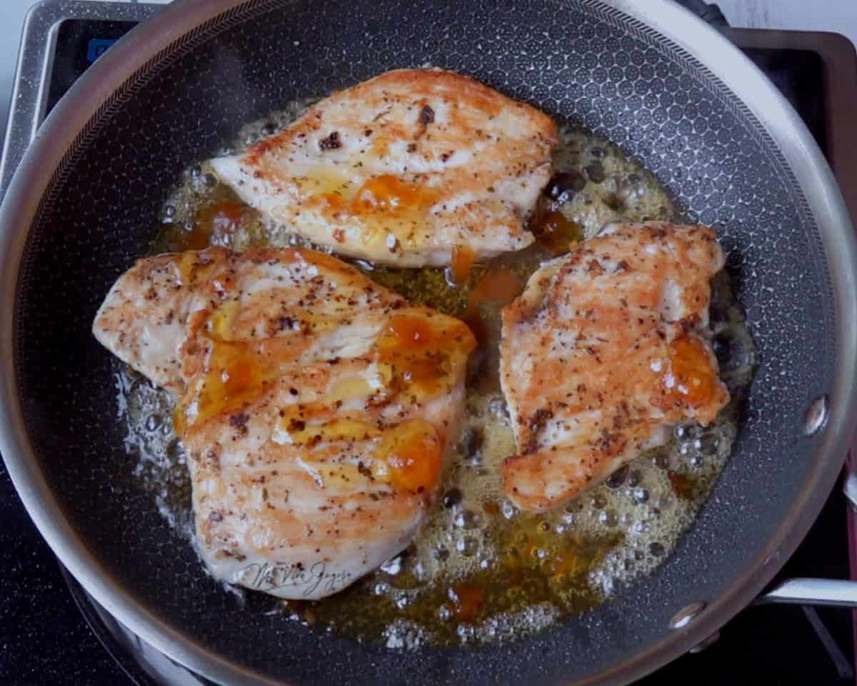 Juicy grilled chicken breasts cooking in a non-stick pan with butter and herbs, perfect for healthy meals and flavorful recipes.