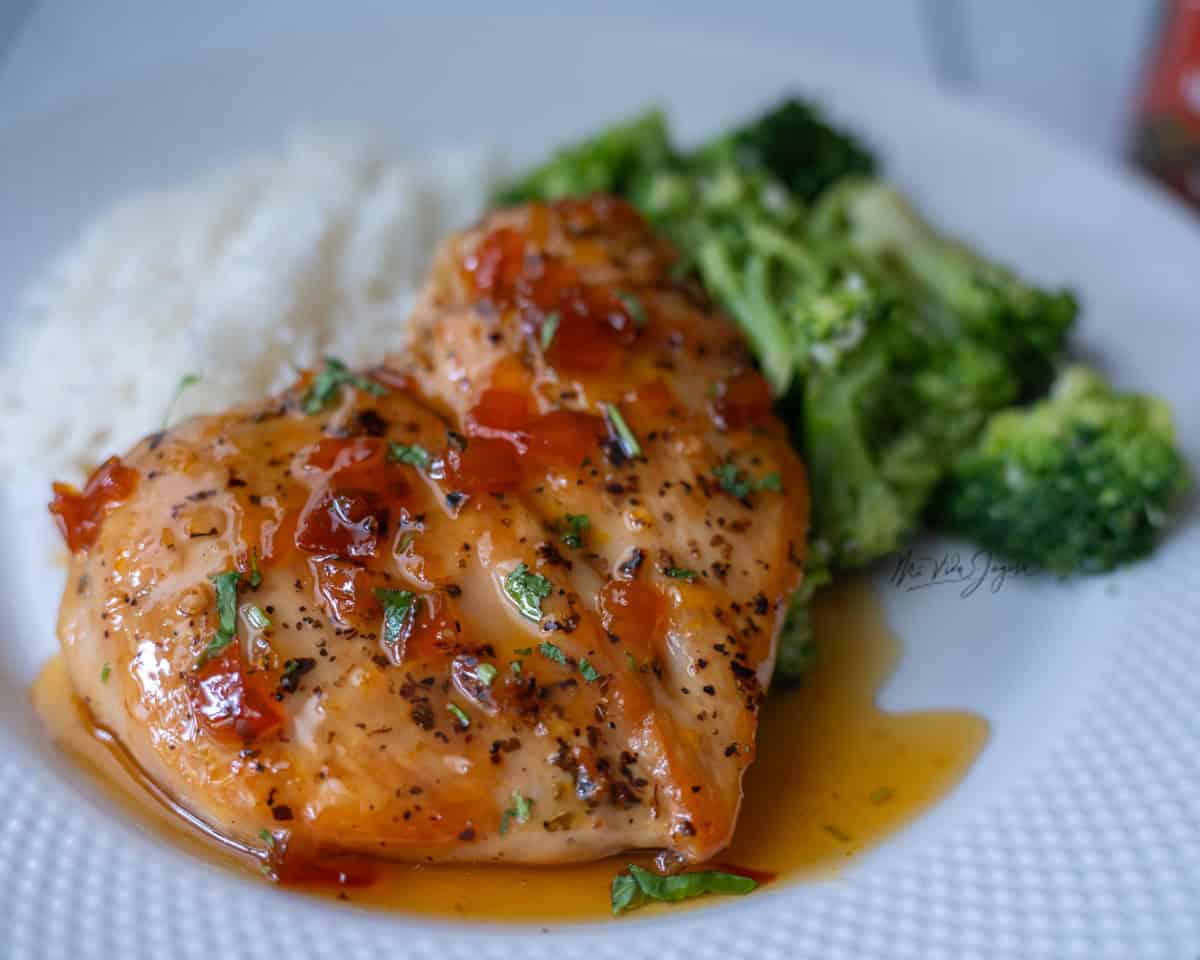 Un plato blanco con arroz servido en el fondo, brocoli a la derecha y pollo a la mermelada en el centro, se observa la mermelada y unos pedacitos de cilantro encima del pollo