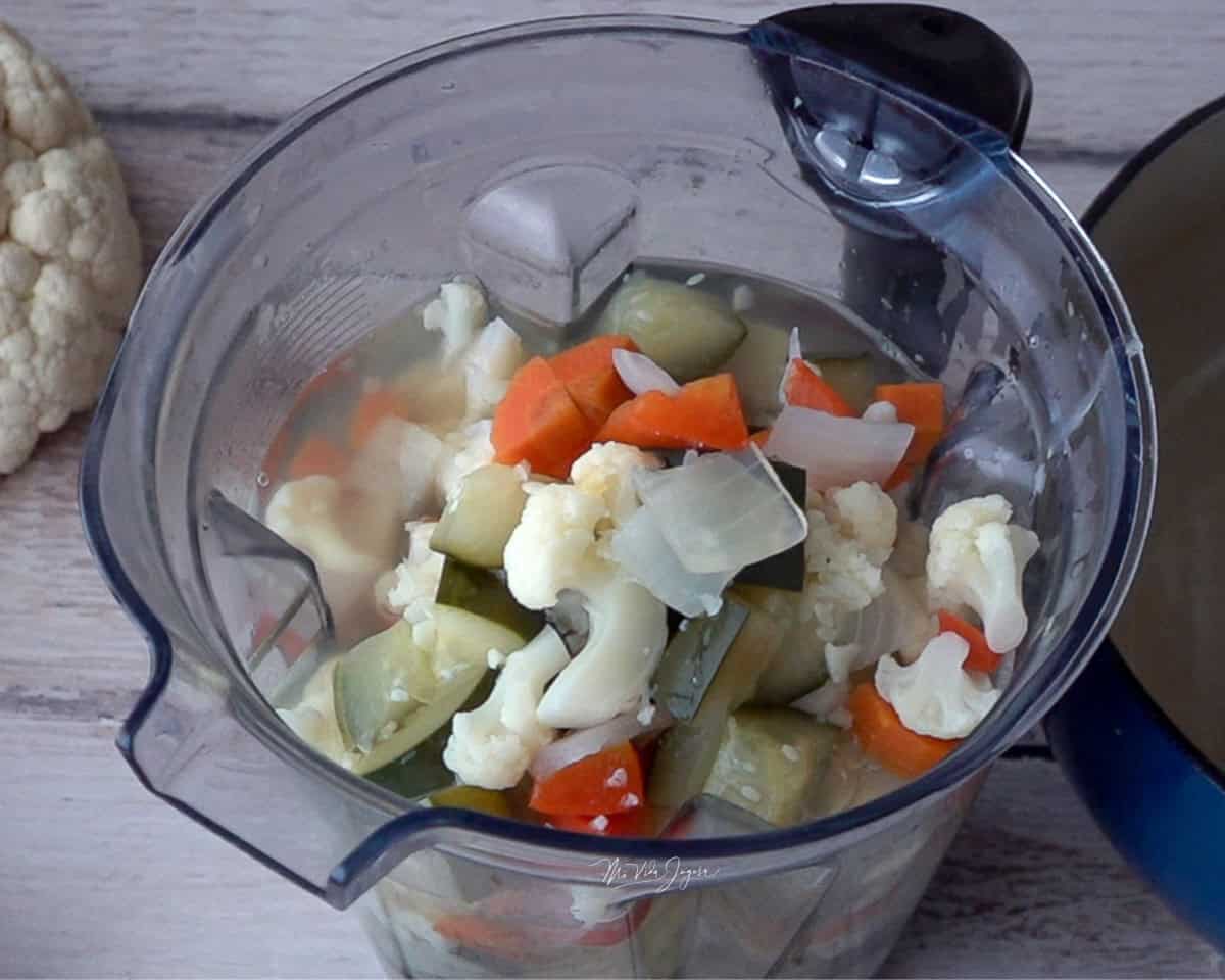 Un pichel de licuadora con los vegetales en cuadritos, junto a una coliflor y una olla.