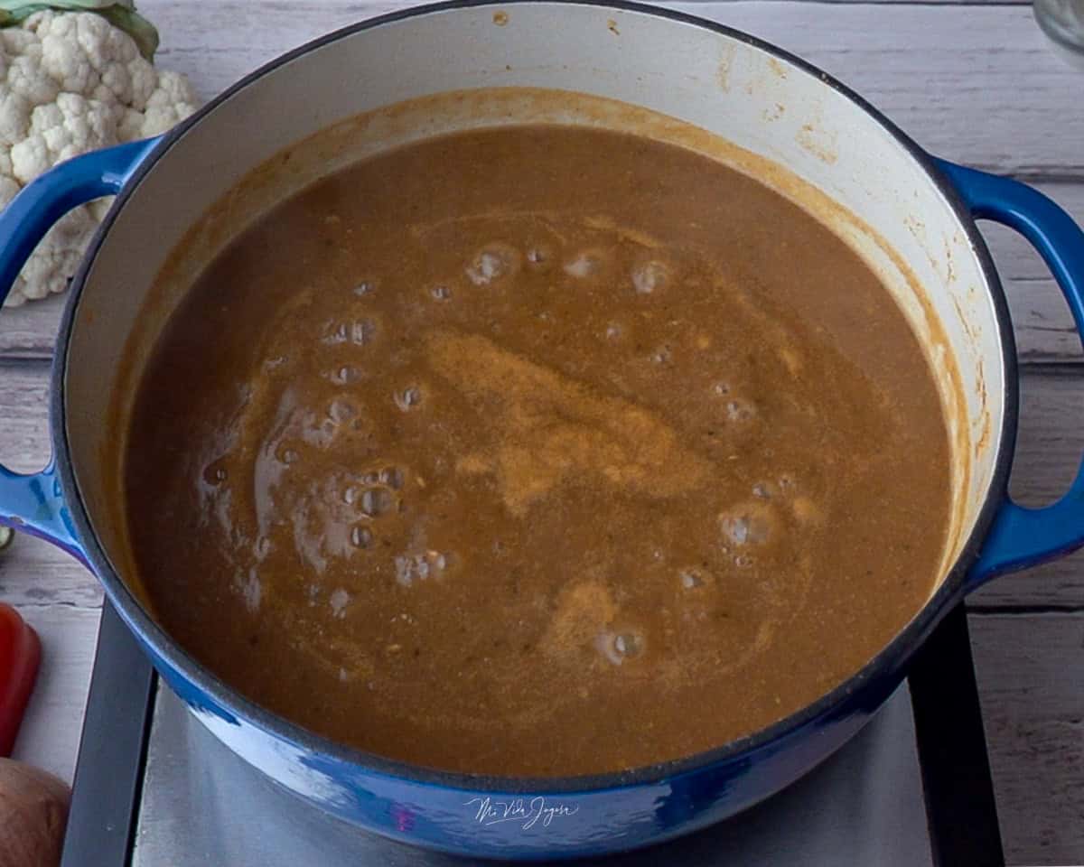 Una olla sobre la cocina con la mezcla líquida en su interior y una coliflor al fondo.